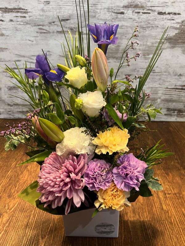 A tall box arrangement including fresh seasonal flowers; lilies, carnations and lissianthus.