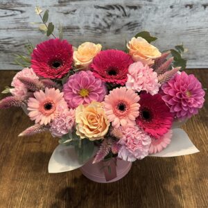 Bright birthday hat box arrangement with pink gerberas, roses and seasonal flowers in a florist choice design