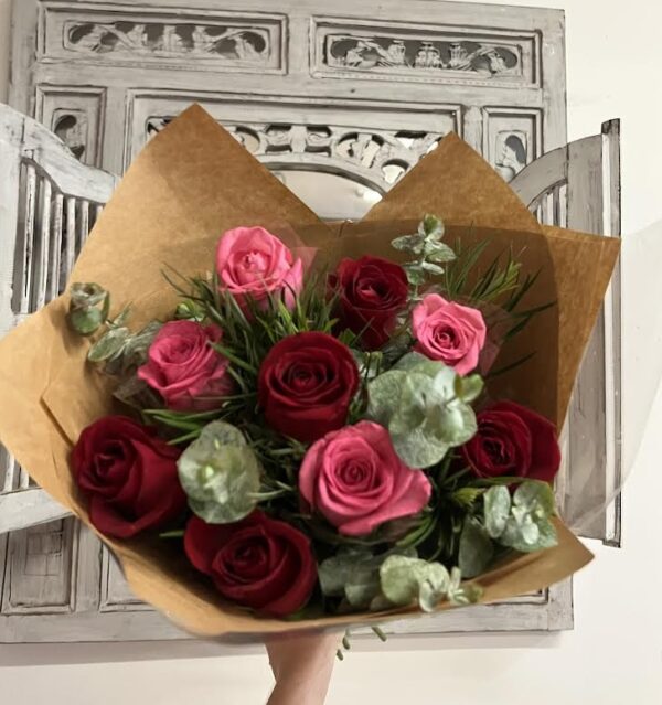 A bouquet of red and pink roses with lush greenery, all wrapped up in beautiful paper.