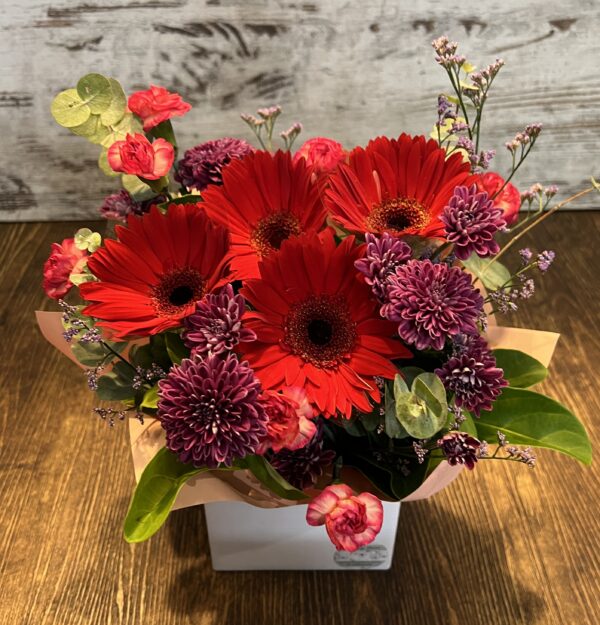 A posy box arrangement of jewel toned gerberas, spray carnations and chrysanthemums.