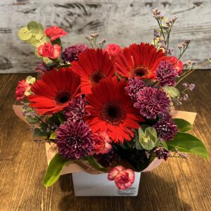 A posy box arrangement of jewel toned gerberas, spray carnations and chrysanthemums.