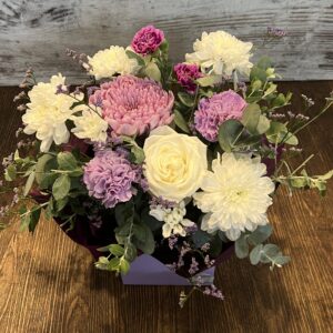A posy box arrangement in purples, mauves and whites. Flowers include gerberas, roses and disbud chrysanthemum.