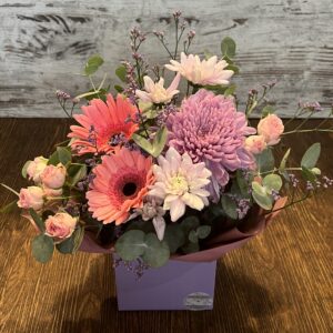 Posy box arrangement in pinks and mauves. Cottages flowers including gerberas, spray roses, disbud chrysanthemum and chrysanthemums.