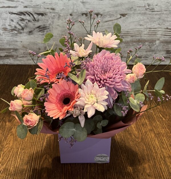 Posy box arrangement in pinks and mauves. Cottages flowers including gerberas, spray roses, disbud chrysanthemum and chrysanthemums.